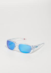 Transparente Sonnenbrille mit blauen Verlaufslinsen, rechteckiger Form und strukturierten klaren Rahmen. Mit Logo an der Seite.