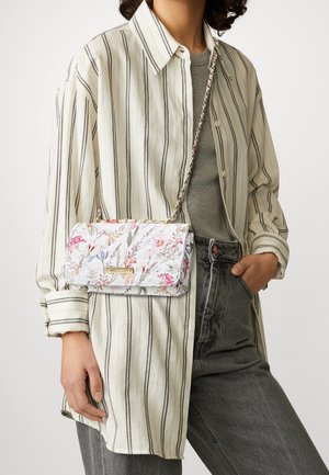 Persoon draagt een gestreept crèmekleurig shirt en grijze jeans, en heeft een bloemenquilted crossbodytas met een gouden kettingband.