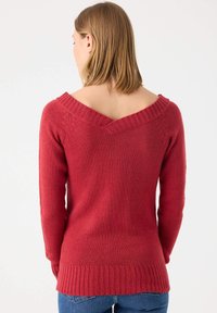 Suéter de punto rojo con mangas largas y un escote en V profundo. Presenta dobladillos acanalados, tejido texturizado y un diseño de espalda alargado.
