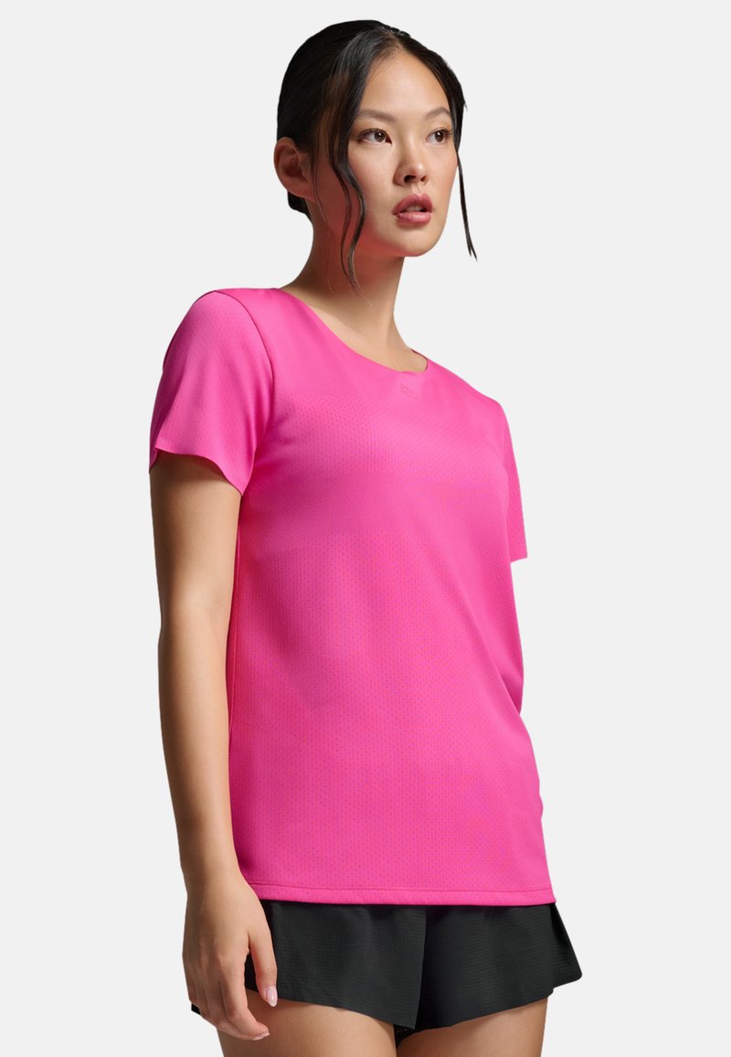 Camiseta deportiva de manga corta en tejido rosa brillante con superficie texturizada, combinada con pantalones cortos negros, con escote redondo.
