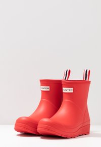 Bottes de pluie en caoutchouc rouges avec une pointe arrondie, un design profilé, des poignées en tissu et un accent rayé noir et blanc en haut.