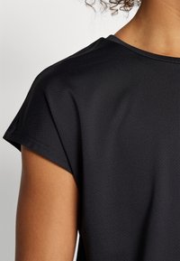 Camiseta deportiva negra con tela texturizada, mangas cortas y un escote ligeramente redondeado, que muestra un acabado suave.