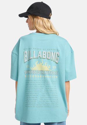 Light blue oversized t-shirt featuring a graphic print of the sun and palm trees on the back, with text detailing locations, cotton material.
