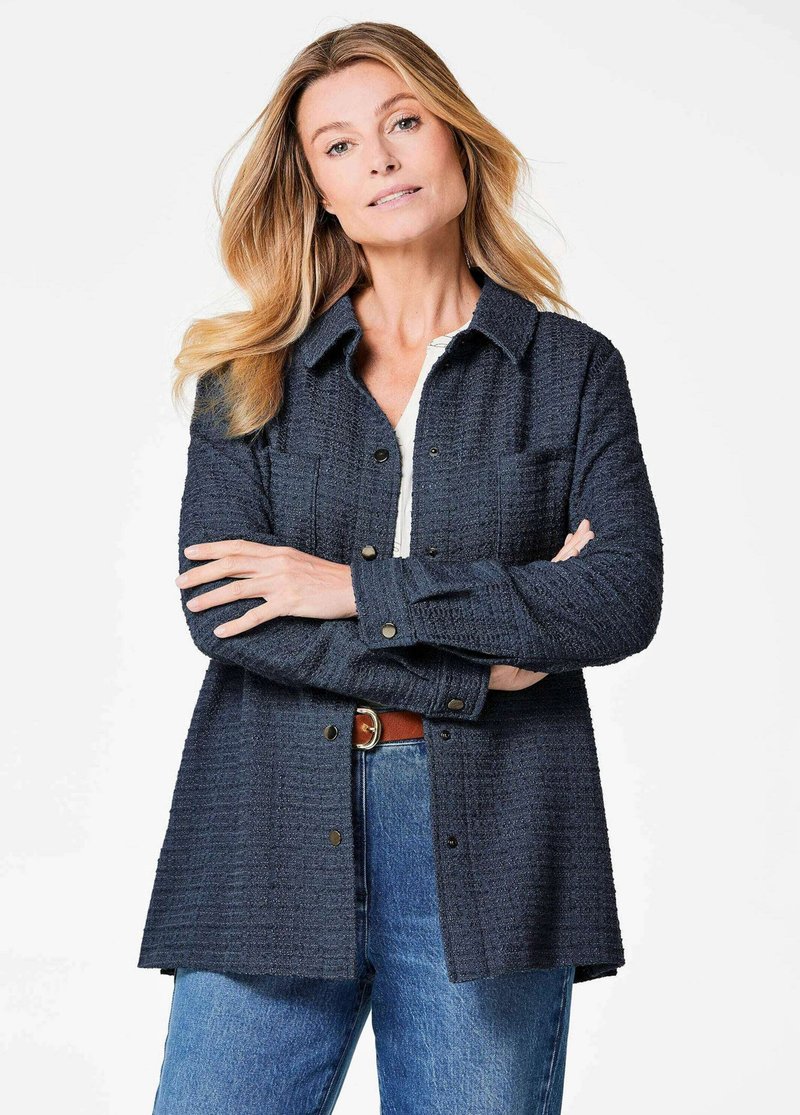 Navy blue textured shirt jacket with a front button closure, pointed collar, and two chest pockets, paired with high-waisted jeans.