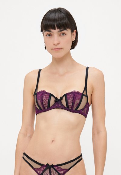 Csipkés bralette és tanga szett, amely lila virágos csipkéből készült fekete kiegészítőkkel, merevítős támasztékkal, áttetsző panelekkel és dekoratív fekete masnichabokkal rendelkezik.