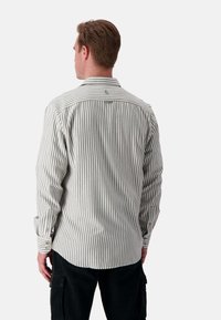 Camicia a maniche lunghe a righe in olivo e crema. Collo button-down, logo sul petto e bottoni ai polsi. Tessuto di cotone morbido con vestibilità sartoriale.