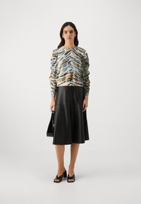 Bluza z dolgimi rokavi z večbarvnim vzorcem tigrovega črta, v kombinaciji z črno usnjeno A-line krilo in črnimi platformnimi sandali.