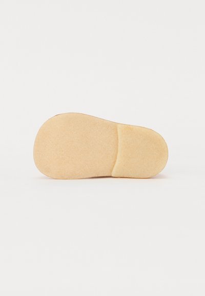 Såle av en sko, med en avrundet form, laget av et lett beige materiale med en myk tekstur og uten synlige mønstre eller detaler.