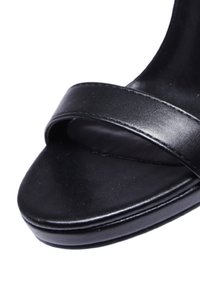 Sandal in pelle nera con una larga fascia sulla punta e una suola liscia e arrotondata. Presenta un tacco basso e massiccio e una finitura lucida.