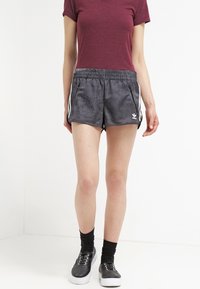 Grå atletiska shorts med pricksömönster, elastisk midjeband, dragkedjefickor och vita sidostråk. Kombineras med en vinröd t-shirt och svarta sneakers.