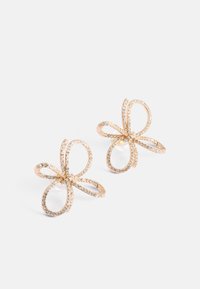 Náušnice ve zlatém tónu ve tvaru květin, s třpytivými detaily a hladkými, zakřivenými liniemi s reflexním povrchem.