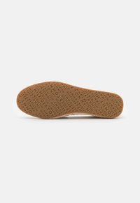 Semelle de chaussure marron clair avec un texte en relief répétitif "TOMMY HILFIGER" sur toute la surface.