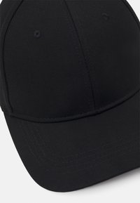 Musta baseball-lippis, jossa on rakenteellinen muotoilu, valmistettu teksturoidusta kankaasta. Siinä on kaareva lippa ja ommeltuja yksityiskohtia. Ei näkyviä logoja.