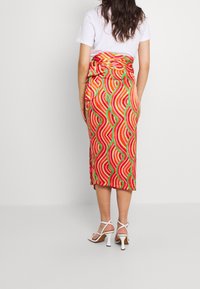 Jupe enveloppante colorée avec un motif ondulé vibrant en rouge, rose et vert, fabriquée dans un tissu léger. Nouée à la taille.