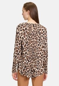 Blusa con stampa maculata in beige, marrone e nero; presenta maniche lunghe, scollatura rotonda con apertura a chiave e dettaglio plissettato sul retro.