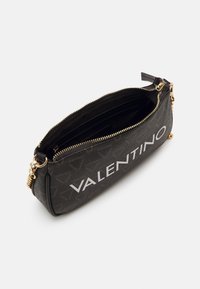 Svart Valentino-väska med en texturerad yta, vitt logotyp, guld blixtlås och en ficka med blixtlås. Kompakt form för enkel bärning.