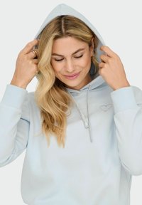 Jasnoniebieska hoodie z miękkiego materiału, z srebrnym sznurkiem i małym serduszkiem haftowanym na piersi. Prążkowane mankiety dopełniają design.