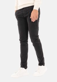 Pantaloni neri slim-fit in cotone. Presentano tasche anteriori, passanti per cintura e una texture liscia. Abbinati a sneakers bianche.