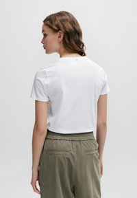 White cotton t-shirt with a crew neckline and short sleeves, seen from behind; paired with olive green elastic-waist pants featuring pockets.