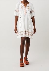 Vit bomullsklänning med puffärmar, broderade blommor, midilång volangkant och framhävd halsringning. Tillsammans med orange plattformshälar.