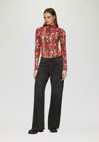 Rood en zwart slangenprint jumpsuit met hoge hals, gecombineerd met zwarte broek met wijde pijpen, voorzien van zijzakken en een gedetailleerde afwerking.