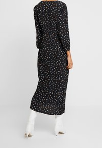 Robe maxi noire à fleurs avec manches longues, présentant un motif floral dispersé en bleu et marron, confectionnée dans un tissu léger.