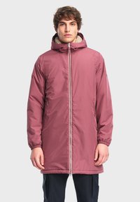 Dlouhá růžová parka s kapucí, která má načechranou podšívku a zapínání na zip v přední části. Viditelné jsou elastické manžety a boční kapsy.