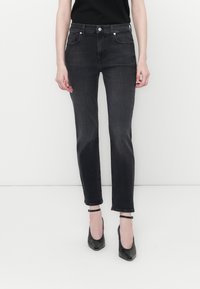Jean en denim de lavage foncé avec une coupe ajustée, taille haute, deux poches avant et petites poches arrière. Fini avec un ourlet retroussé et un bouton métallique.