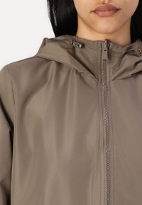 Lichte, bruine hoodie met een volledige rits aan de voorkant, verstelbaar trekkoord bij de capuchon en een gladde, licht glanzende textuur.