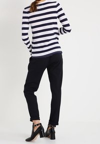 Koszula w paski w kolorze granatowym i białym z długim rękawem, połączona z czarnymi spodniami o podwiniętych nogawkach. Czarne buty na obcasie z kostkowymi paskami. Gładka tekstura tkaniny.