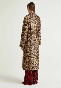 Vestaglia lunga con stampa leopardata e cintura, realizzata in tessuto liscio. Presenta un collo sciallato e maniche ampie, abbinata a pantaloni larghi a gamba larga con stampa floreale rossa.