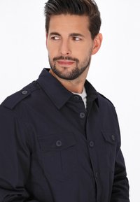 Dunkelblaue Baumwollhemd mit Knopfleiste, Verbreiteter Kragen, zwei Brusttaschen und Schulterklappen. Weiche Textur und einfarbig.