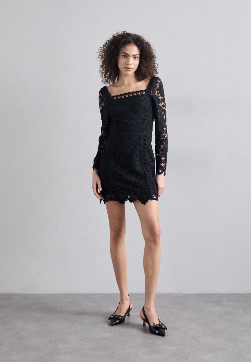 Czarna koronkowa sukienka z długimi rękawami, kwadratowym dekoltem, skomplikowanymi wzorami kwiatowymi i falbanistym dołem. Połączona z czarnymi butami na obcasie.