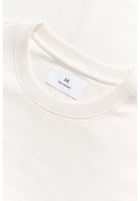 Bílá bavlněná mikina s vroubkovaným kulatým krkem a přišitým štítkem s názvem značky "Martinique." Hladká textura, jednoduchý design.