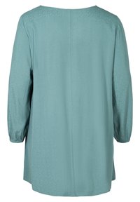 Blouse bleu sarcelle clair en tissu doux, avec manches longues à poignets élastiques, un col rond et un motif texturé subtil.