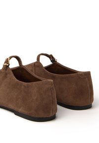 Scarpe in suede marrone con profilo basso, caratterizzate da un piccolo tacco e fibbie in tonalità oro sul retro, interni lisci e forma arrotondata.