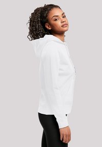 Hvit genser med hette, snøring, frontlomme og ribbestrikkede mansjetter. Bæres med sorte leggings, som har en glatt og myk tekstur.