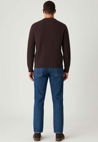 Maglione marrone a treccia con scollo rotondo, abbinato a jeans blu. Polsini e orlo a coste visibili, indossato con scarpe marroni.