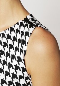 Mustavalkoinen houndstooth-kangasmateriaali, jossa on teksturoitu pinta ja vetskari olkapäällä.