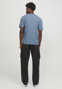 Camiseta azul de algodón de manga corta combinada con pantalones cargo negros que cuentan con bolsillos laterales, ajuste relajado y zapatillas blancas en contraste.