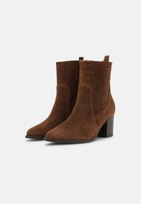 Bottines en daim marron avec un bout pointu, un talon bloc moyen et des détails de couture sur le côté. Texture lisse avec des languettes de tirage en haut.