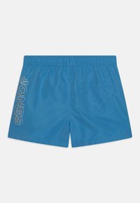 Blauwe zwembroek van lichtgewicht stof heeft een elastische tailleband, een achterzak en grote witte "JONES" tekst aan de zijkant.