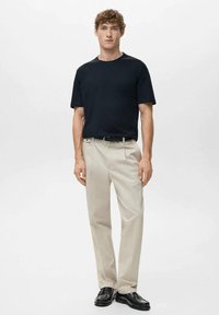 Czarny t-shirt z krótkim rękawem, beżowe spodnie wizytowe, czarny pasek i czarne buty. Strój cechuje się klasycznym krojem i gładką fakturą.