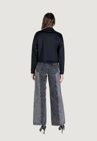 Giacca nera tagliata con una superficie liscia, abbinata a jeans grigi a vita alta e a gamba larga, con un aspetto sbiadito e cuciture visibili.