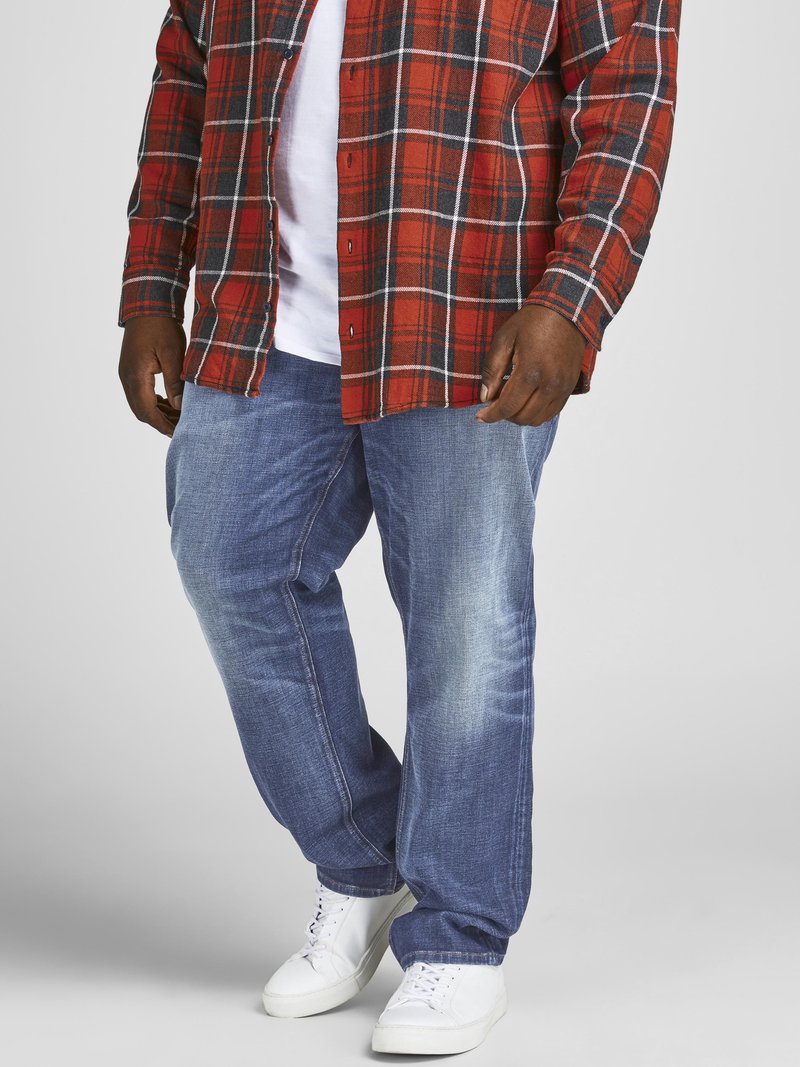 Cămașă cu carouri roșii și negre purtată peste un tricou alb, asociată cu blugi din denim albastri și adidași albi. Aspect casual, confortabil, cu texturi vizibile.