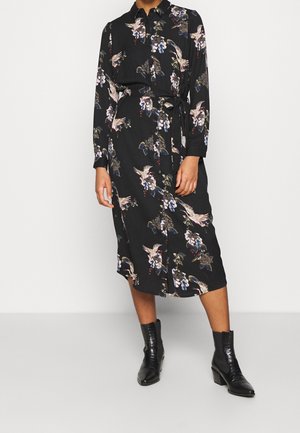 Musta mekko, jossa on kukkakuvio vaaleanpunaisena, sinisenä ja vihreänä. Mekossa on pitkät hihat, kaulus ja vyöllinen vyötärö, ja se ulottuu polven puoliväliin.