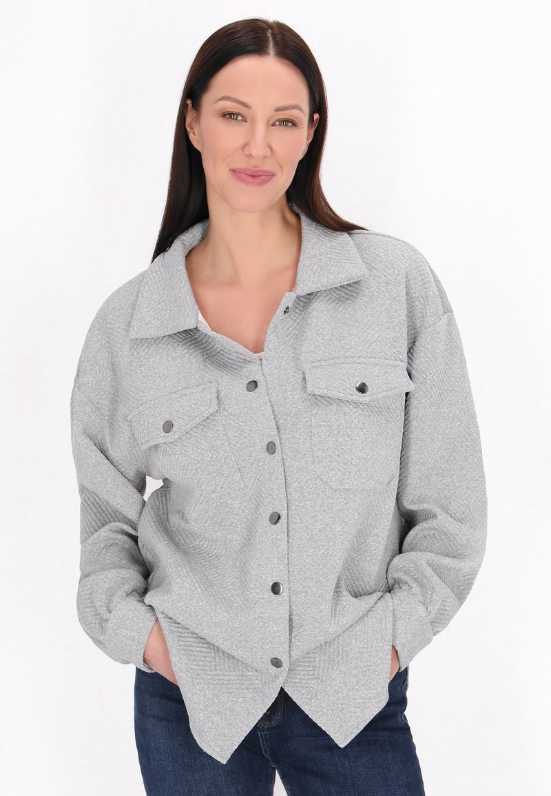 Camicia grigia con colletto strutturato, due tasche sul petto e tessuto testurizzato. Abbinata a jeans scuri, presenta una vestibilità rilassata.