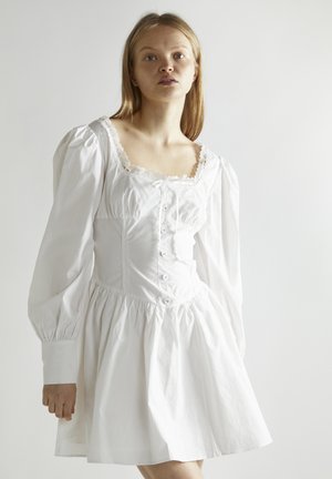 Weißes Kleid mit Puffärmeln, quadratischem Ausschnitt, Spitzenbesatz, Knopfleiste vorne und gerafftem Rock. Hergestellt aus leichtem Baumwollstoff.