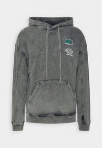 Sudadera gris con un acabado texturizado, bolsillo tipo canguro en la parte frontal, capucha con cordón y logotipos en el pecho. Mangas largas con puños acanalados.