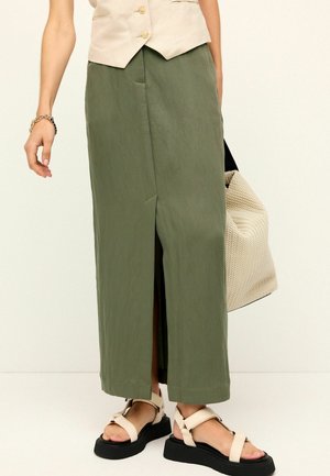 Gonna maxi verde oliva con spacco frontale, realizzata in tessuto leggero. Abbinata a sandali beige e una borsa a tracolla color crema con texture.